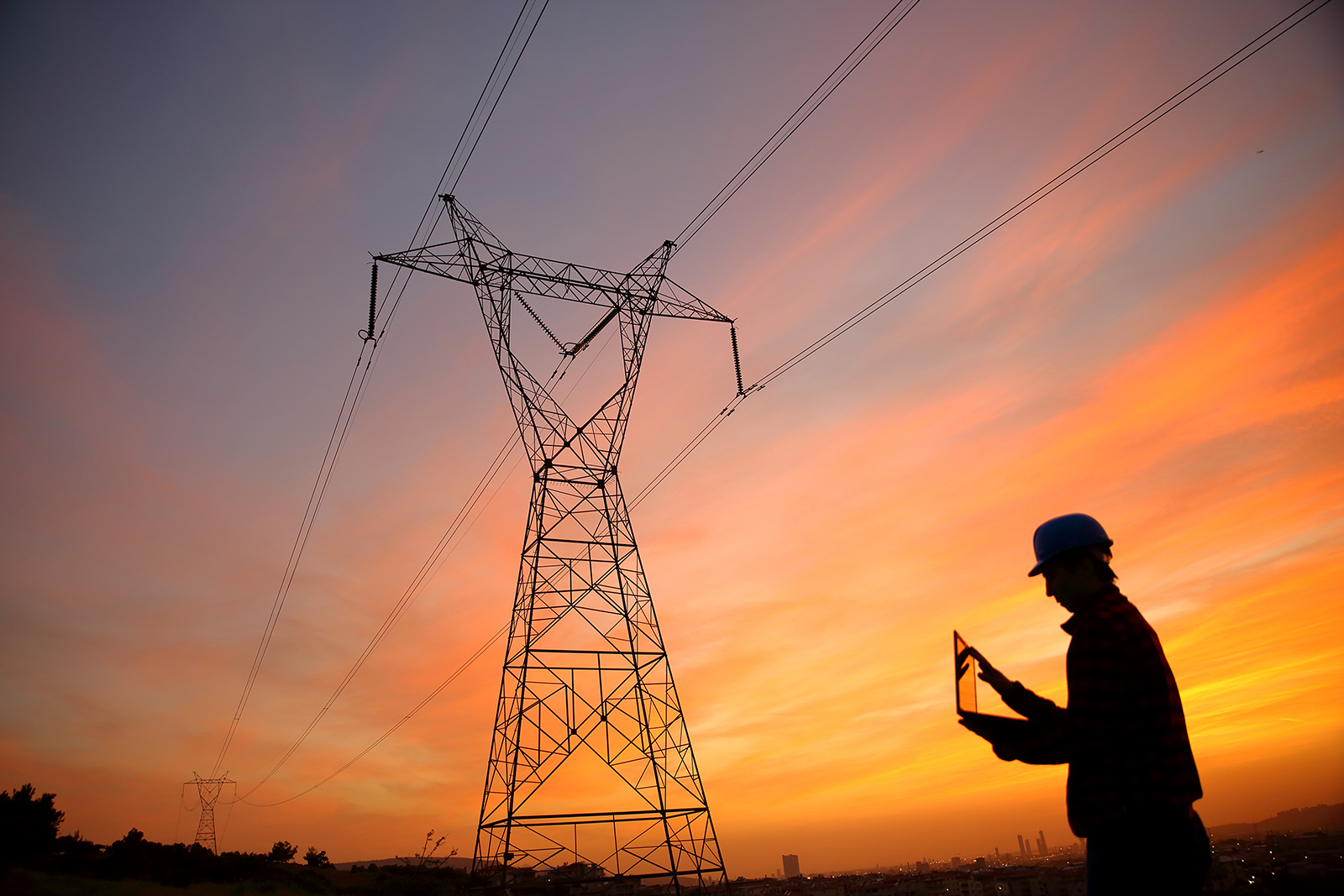 engineer on laptop in shadow of transmission lines