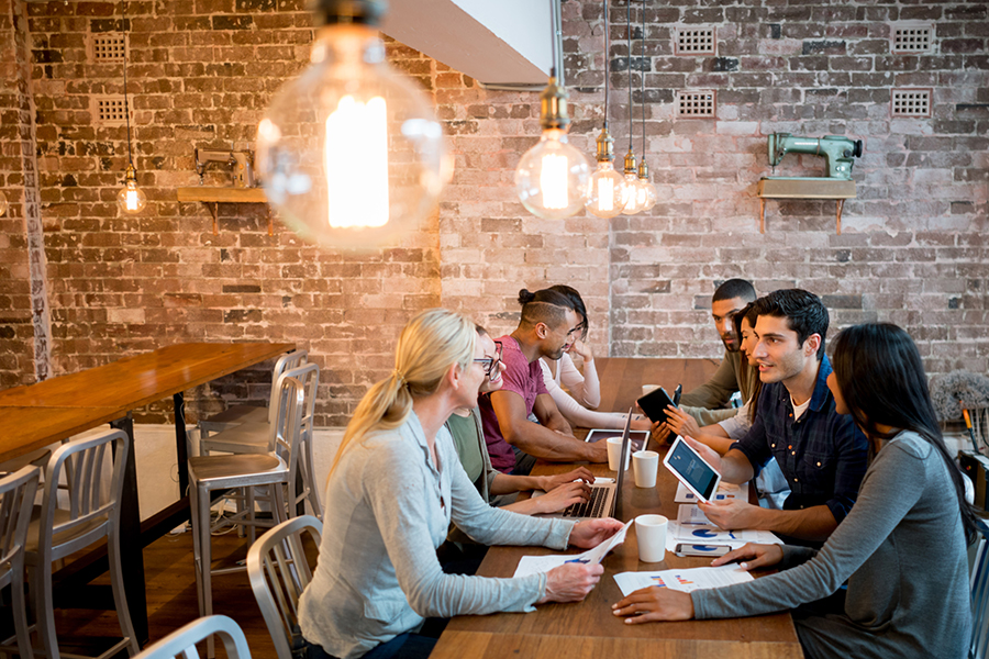 Group of people working at the office sharing ideas and looking very happy with focus on foreground on a lightbulb